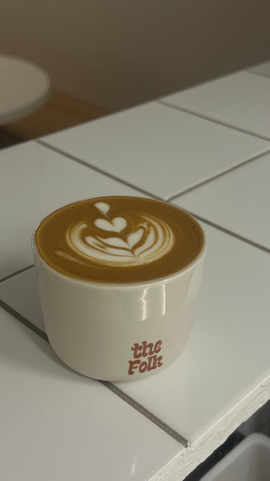 white cup of coffee with the folk logo and nice latte art