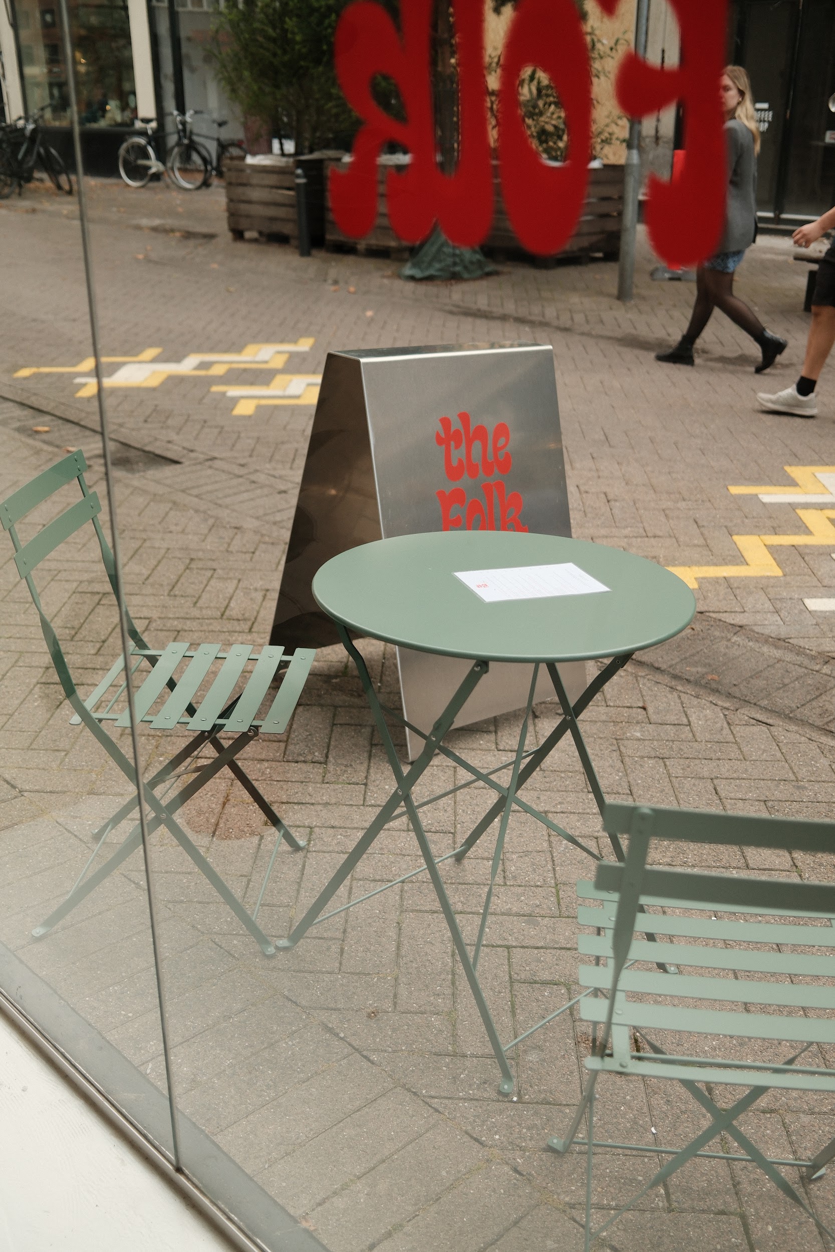 outdoor green chairs table and the folk sign behind a glass wall